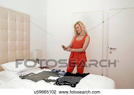 Mature woman in bedroom using smartphone to photograph clothing on bed View Large Photo Image Stock Image - Mature woman in bedroom using smartphone to photograph clothing on bed. Fotosearch