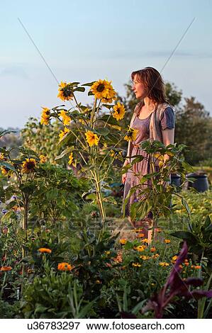 Stock Photo - Mature woman standing in garden, pensive expression. Fotosearch