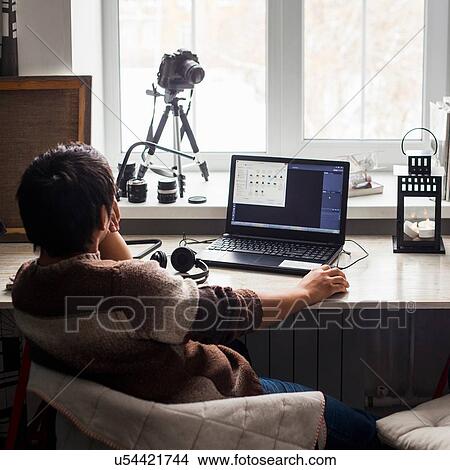 Picture - Mid adult man sitting at desk using laptop, rear view. Fotosearch