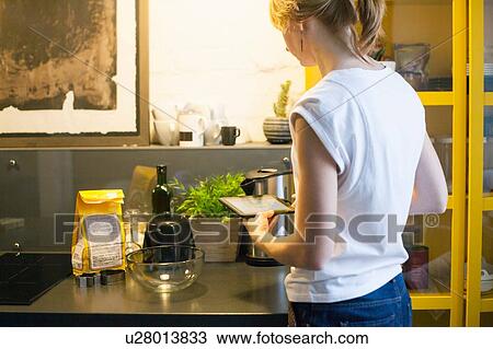 Stock Image - Mid adult woman reading recipe on digital tablet at kitchen counter. Fotosearch