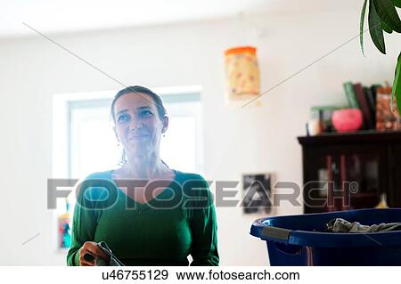 Stock Photo - Mid adult woman sorting clothing in laundry basket, looking away smiling. Fotosearch