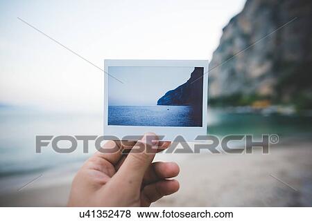 Stock Photo - Person holding up photograph of scene at Lake Garda, Italy. Fotosearch