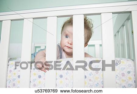 Portrait of baby girl looking through bars on cot View Large Photo Image Stock Photo - Portrait of baby girl looking through bars on cot. Fotosearch