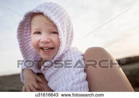 Stock Image - Portrait of female toddler between fathers legs on beach. Fotosearch