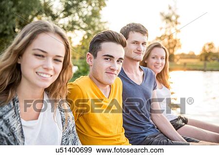 Stock Photo - Portrait of group of friends sitting beside lake, smiling. Fotosearch