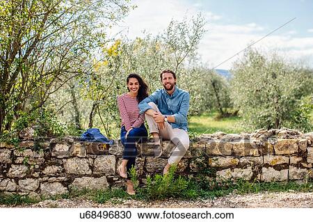 Portrait of young couple sitting on wall in olive grove, Florence, Italy View Large Photo Image Stock Image - Portrait of young couple sitting on wall in olive grove, Florence, Italy. Fotosearch