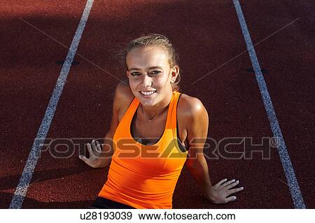Stock Photo - Portrait of young female runner sitting on race track. Fotosearch