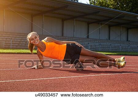 Stock Photo - Portrait of young female runner balancing on side at race track. Fotosearch