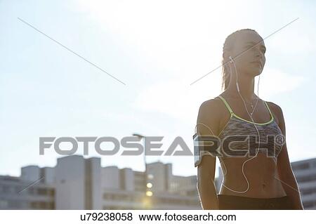 Stock Photo - Portrait of young female runner listening to earphone music on urban rooftop. Fotosearch