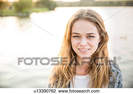 Stock Image - Portrait of young woman beside lake, smiling. Fotosearch