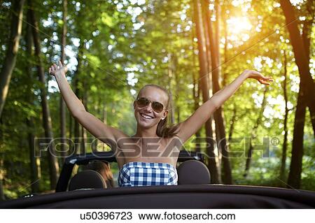 Stock Image - Portrait of young woman in back seat of convertible car. Fotosearch