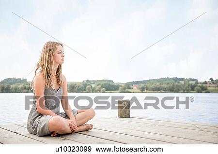 Portrait of young woman sitting on jetty, crossed legs View Large Photo Image Stock Photo - Portrait of young woman sitting on jetty, crossed legs. Fotosearch