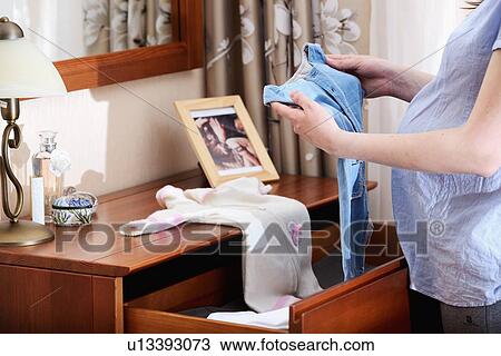 Stock Image - Pregnant woman holding baby clothes, mid section. Fotosearch