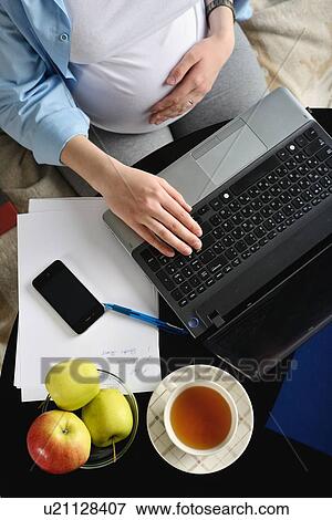 Stock Photo - Pregnant woman sitting on sofa, using laptop, overhead view. Fotosearch