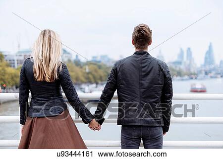 Stock Image - Rear view of romantic young couple in front of Thames river, London, England, UK. Fotosearch