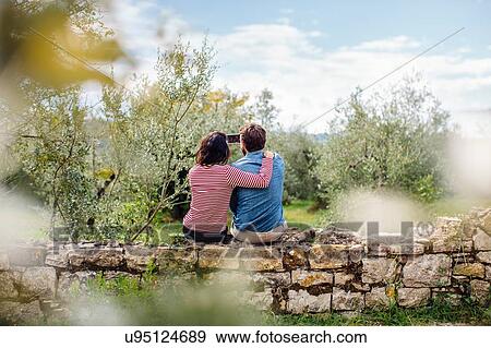 Stock Photo - Rear view of young couple taking smartphone selfie in olive grove, Florence, Italy. Fotosearch