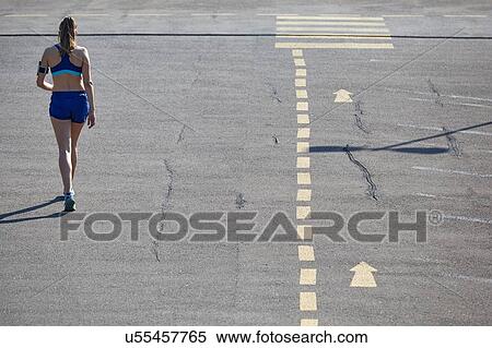Stock Photography - Rear view of young female runner running in parking lot. Fotosearch
