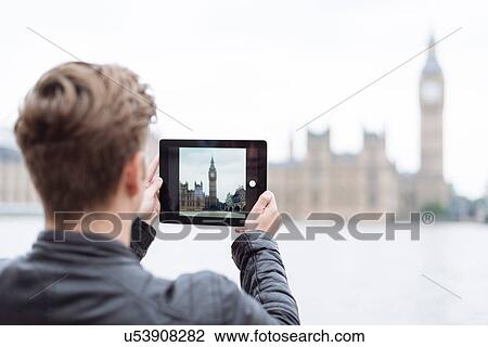 Stock Image - Rear view of young man photographing Big Ben on digital tablet, London, England, UK. Fotosearch