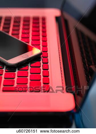 Stock Image - Red light on laptop and mobile phone illustrating danger from hackers. Fotosearch