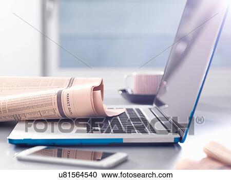 Stock Image - Reviewing financial affairs with newspaper market data page sitting on a laptop computer. Fotosearch