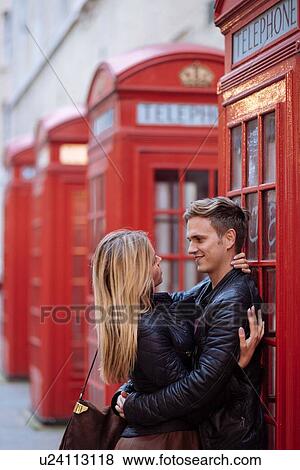 Stock Photo - Romantic young couple hugging next to red phone boxes, London, England, UK. Fotosearch