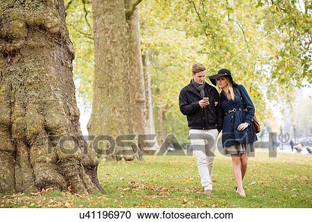 Stock Image - Romantic young couple reading smartphone texts in park, London, England, UK. Fotosearch