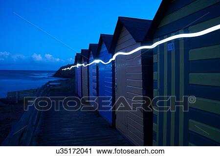 Stock Image - Row of colourful beachhuts at dusk, with light trail, Bude, Cornwall, UK. Fotosearch