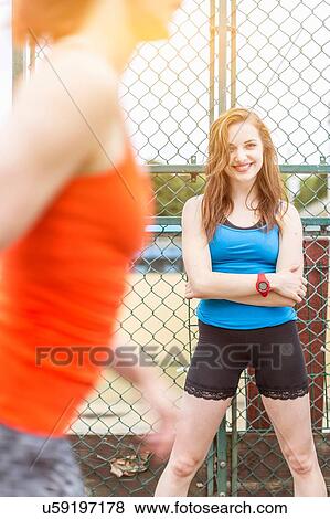 Runner passing young woman standing beside sports ground, London, UK View Large Photo Image Stock Photo - Runner passing young woman standing beside sports ground, London, UK. Fotosearch