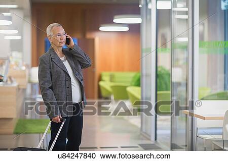 Senior businesswoman with wheeled suitcase chatting on smartphone in hotel lobby View Large Photo Image Stock Image - Senior businesswoman with wheeled suitcase chatting on smartphone in hotel lobby. Fotosearch