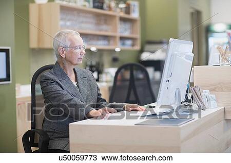 Senior female receptionist using desktop computer at hotel reception desk View Large Photo Image Stock Image - Senior female receptionist using desktop computer at hotel reception desk. Fotosearch
