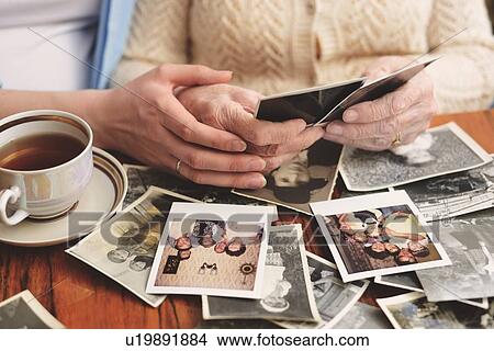 Senior woman and granddaughter sitting at table, looking through old photographs, mid section View Large Photo Image Picture - Senior woman and granddaughter sitting at table, looking through old photographs, mid section. Fotosearch
