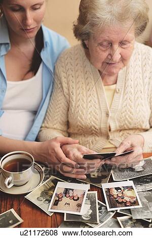 Senior woman and granddaughter sitting at table, looking through old photographs View Large Photo Image Stock Photo - Senior woman and granddaughter sitting at table, looking through old photographs. Fotosearch