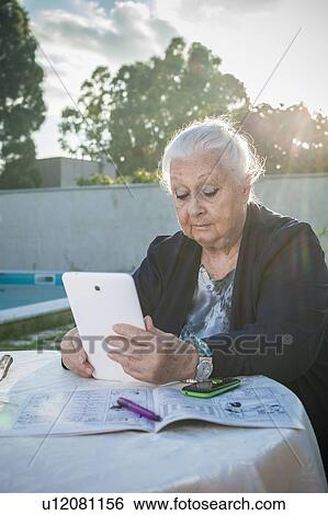 Stock Photograph - Senior woman using digital tablet in backyard. Fotosearch
