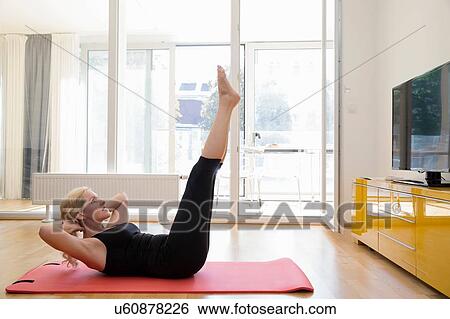 Side view of mature woman lying on back on yoga mat, hands behind head, legs raised exercising View Large Photo Image Stock Photograph - Side view of mature woman lying on back on yoga mat, hands behind head, legs raised exercising. Fotosearch