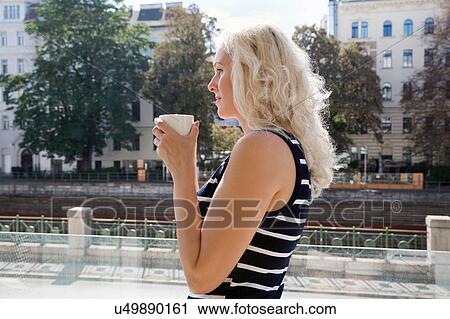 Stock Image - Side view of mature woman outdoors holding coffee cup looking away. Fotosearch