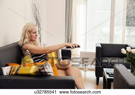 Side view of mature woman sitting on sofa pointing remote control, looking away smiling View Large Photo Image Stock Image - Side view of mature woman sitting on sofa pointing remote control, looking away smiling. Fotosearch