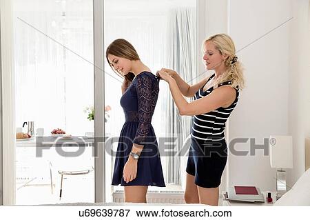 Side view of woman in bedroom helping friend wearing dress to fasten back View Large Photo Image Stock Photo - Side view of woman in bedroom helping friend wearing dress to fasten back. Fotosearch