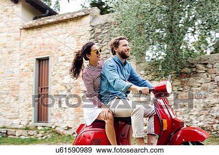 Stock Photo - Side view of young couple riding moped in village, Florence, Italy. Fotosearch