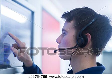 Side view of young man wearing headset using touch screen computer monitor View Large Photo Image Stock Photography - Side view of young man wearing headset using touch screen computer monitor. Fotosearch