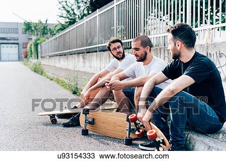 Side view of young men sitting on kerb with skateboards View Large Photo Image Stock Image - Side view of young men sitting on kerb with skateboards. Fotosearch
