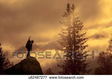 Stock Photo - Silhouetted view of male looking down from rock at sunset, Ural, Russia. Fotosearch