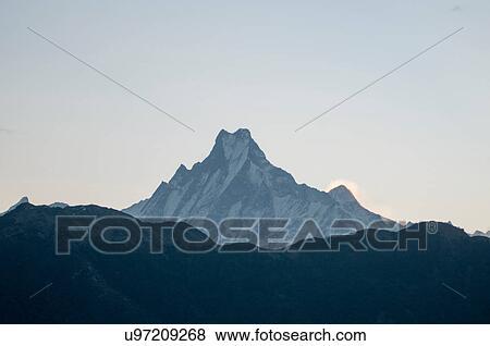 Stock Photo - Snow capped mountain peak against dark mountain range, Nepal. Fotosearch