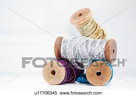 Stock Photography - Stack of wooden reel with sparkly silver, gold, blue and purple ribbons. Fotosearch