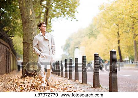 Stylish young man strolling through autumn leaves in city park View Large Photo Image Stock Image - Stylish young man strolling through autumn leaves in city park. Fotosearch