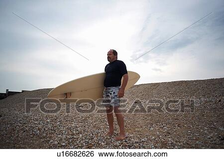 Stock Photograph - Surfer carrying surfboard on beach. Fotosearch