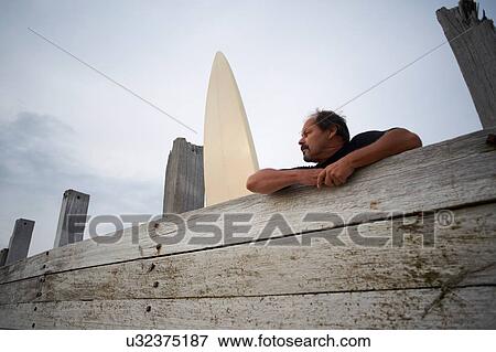 Stock Photo - Surfer leaning against wooden fence with surfboard. Fotosearch