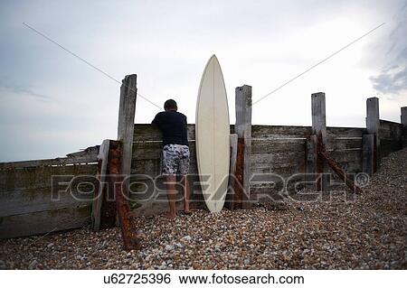 Surfer leaning against wooden fence with surfboard View Large Photo Image Stock Photograph - Surfer leaning against wooden fence with surfboard. Fotosearch