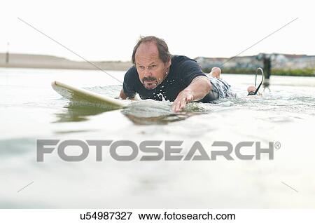Surfer paddling surfboard out to sea View Large Photo Image Stock Photo - Surfer paddling surfboard out to sea. Fotosearch