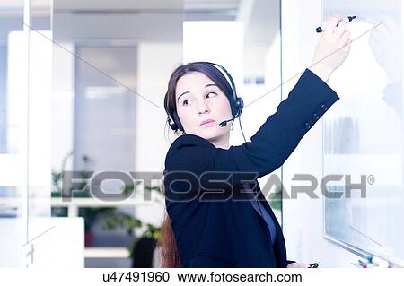 Stock Image - Telephonist writing on whiteboard in office. Fotosearch