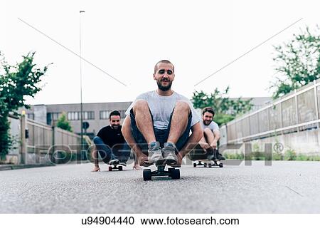 Stock Image - Three young men sitting on skateboards. Fotosearch